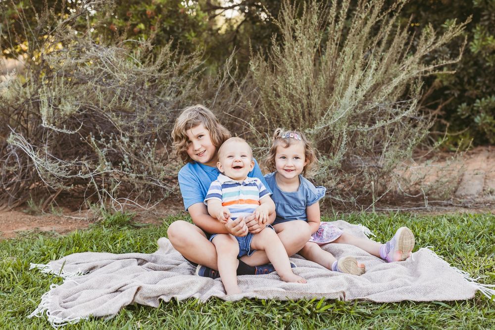 A family relaxes together on a blanket outdoors during a sunny afternoon photo session.