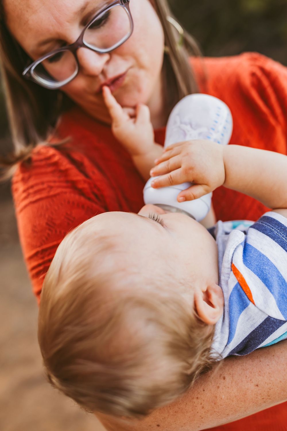 A parent in an orange sweater cradles and nurses a baby wearing blue and white stripes.