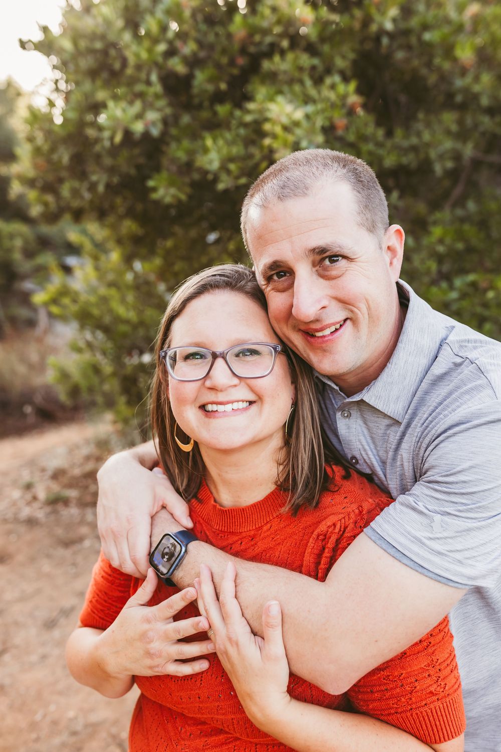 A couple shares a playful moment while embracing outdoors in red and grey casual attire.
