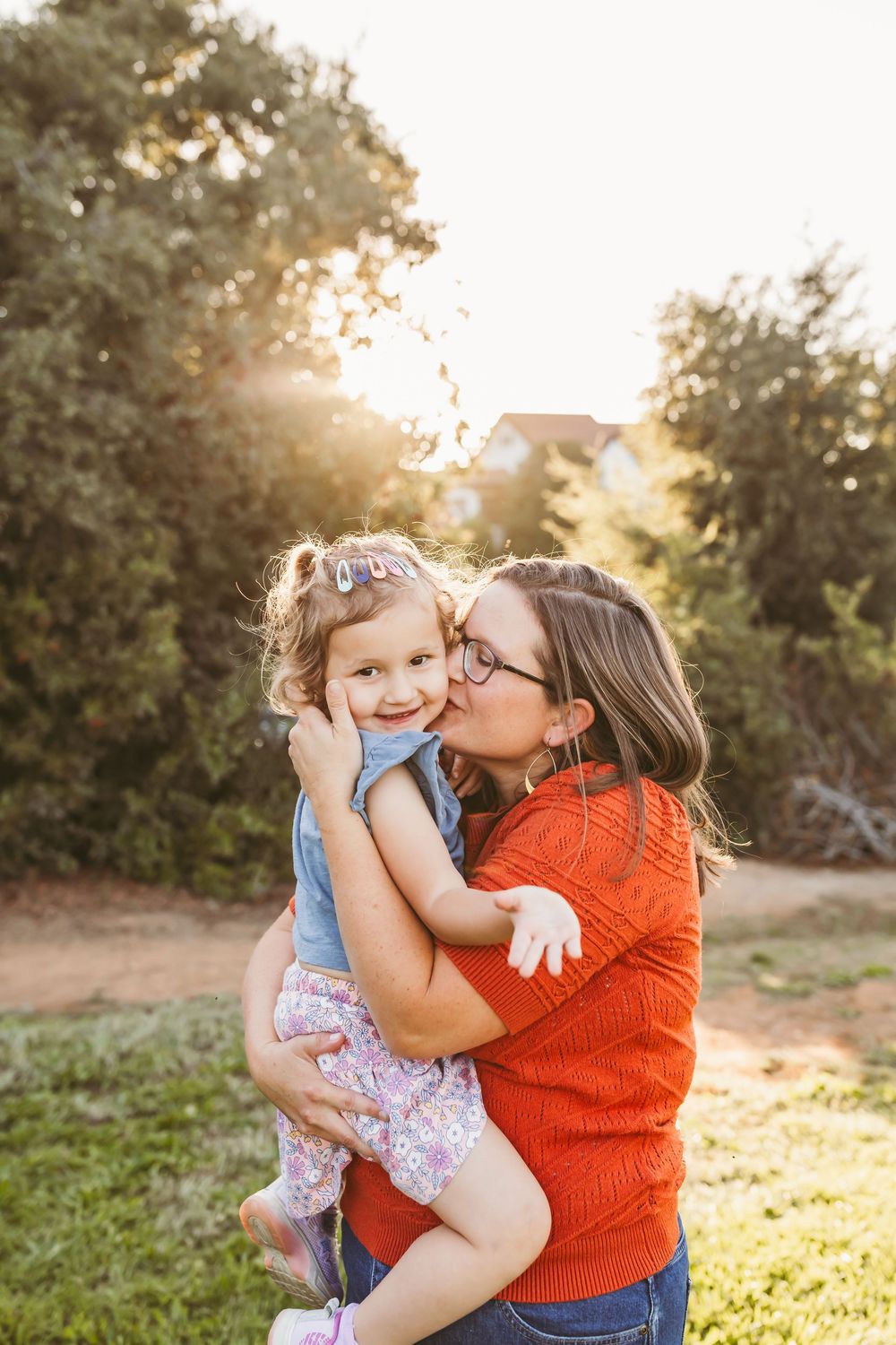 A tender family moment captured in warm sunlight as they share hugs and smiles outdoors.