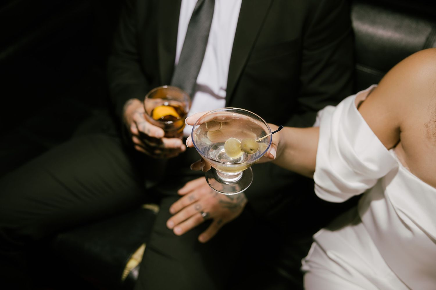 Two people sitting close together holding cocktail glasses and snacks at an elegant event.