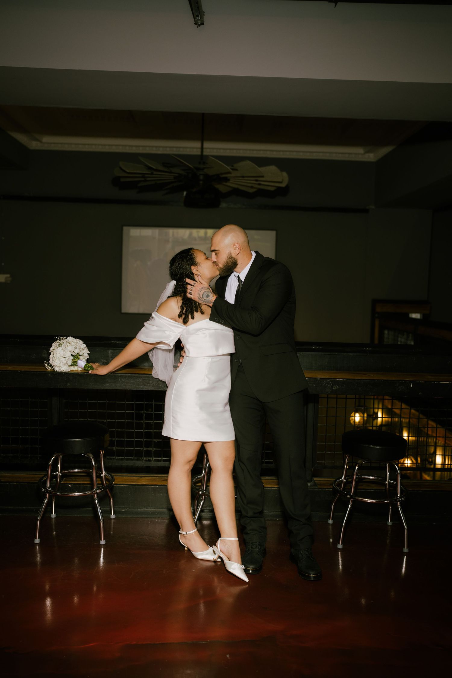 A couple shares an intimate dance move in a dimly lit venue with chairs in the background.