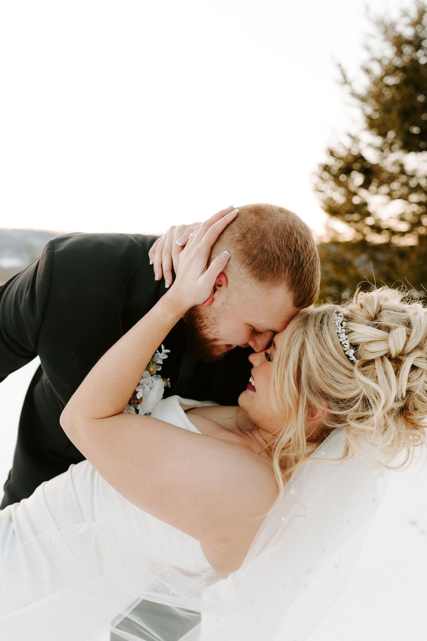 Groom dips bride for romantic kiss during outdoor winter wedding portrait session in the snow.