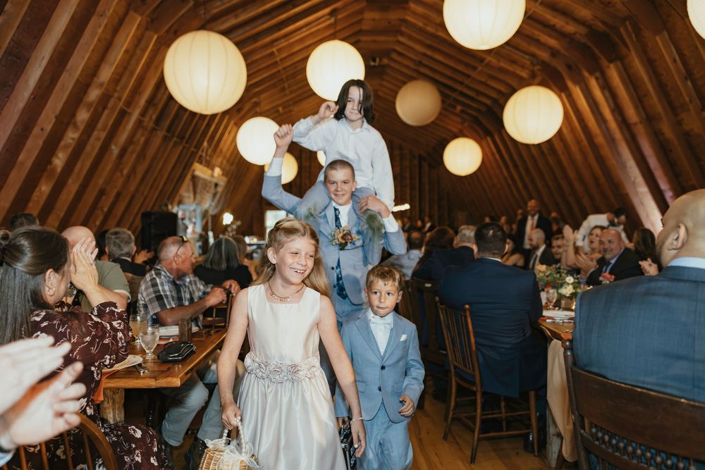 Wedding reception in rustic barn venue with glowing paper lanterns and guests dancing on wooden floor.