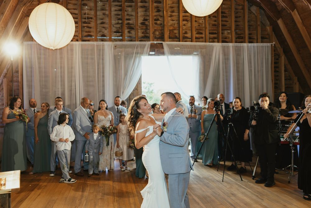 Wedding guests dance together in a rustic barn venue illuminated by glowing paper lanterns during an evening reception.