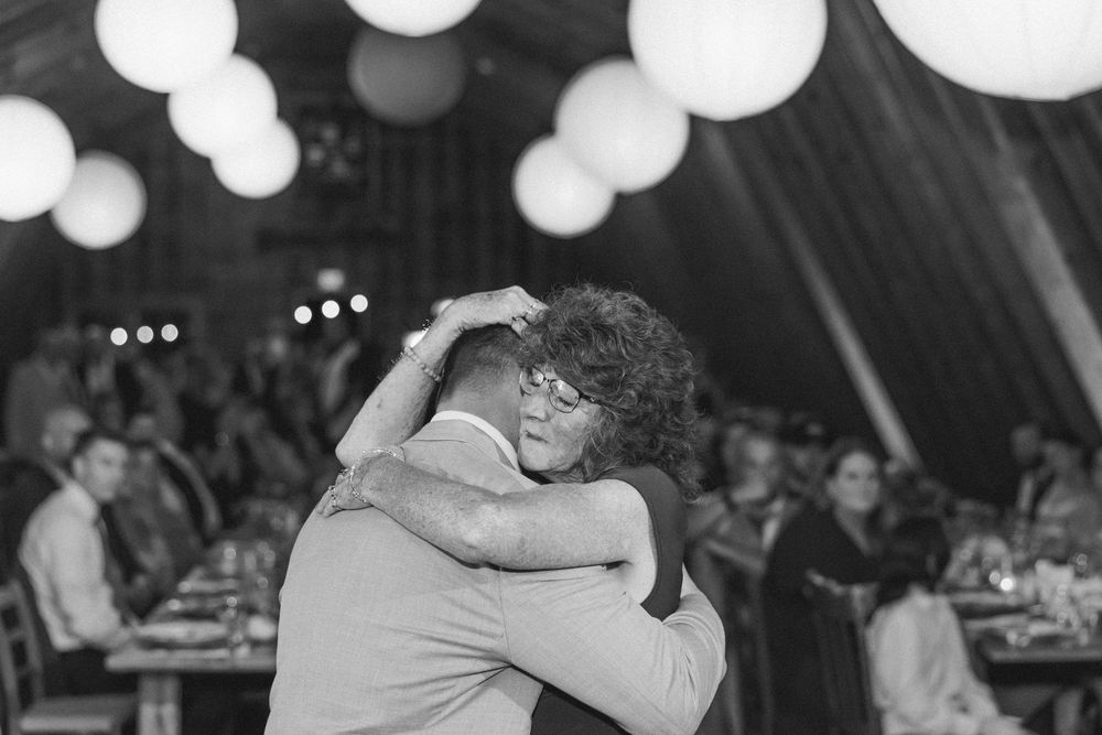 Wedding guests dance and celebrate under glowing paper lanterns in a rustic barn venue.
