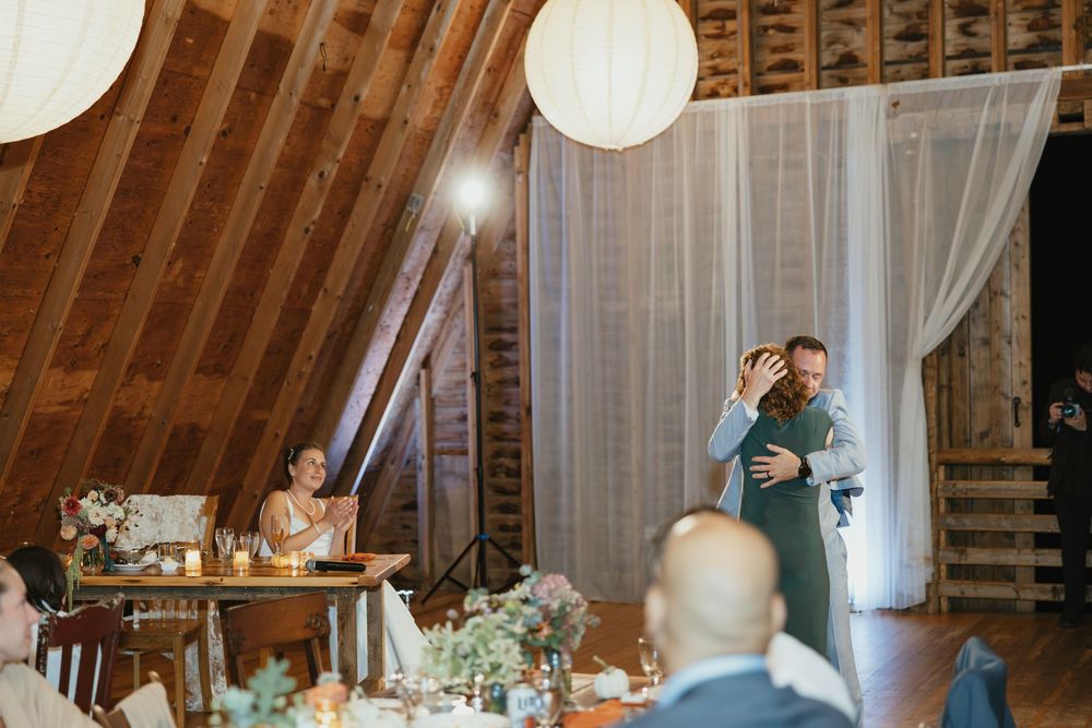 Wedding reception in a rustic barn venue with paper lanterns and sheer white drapes decorating the wooden rafters.