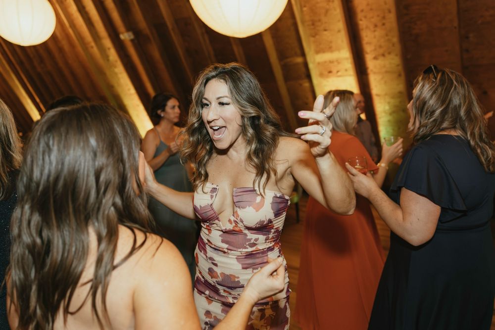 Wedding guests dancing together under glowing paper lanterns in a rustic wooden venue.