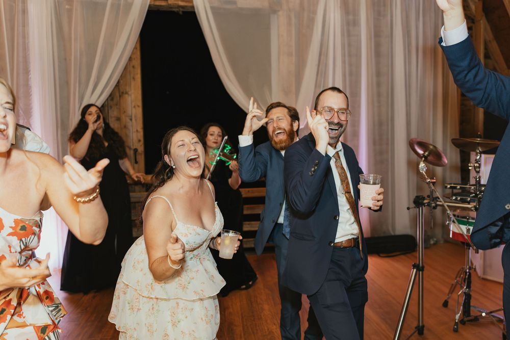 Wedding guests dancing enthusiastically together at a reception with sheer curtains in the background.