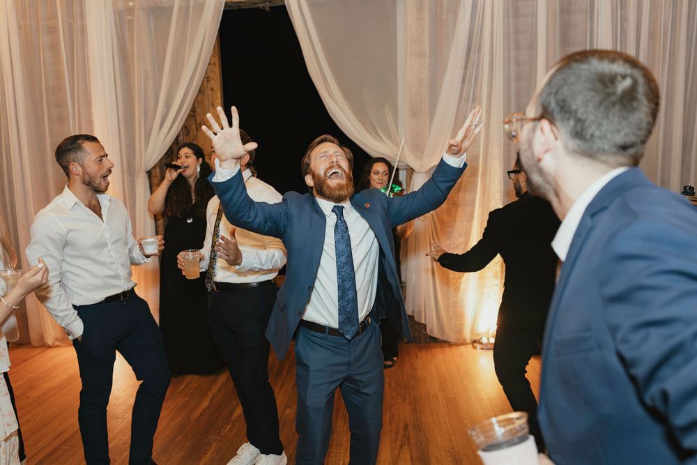 Wedding party dancing in an elegant venue with sheer curtains and warm lighting.