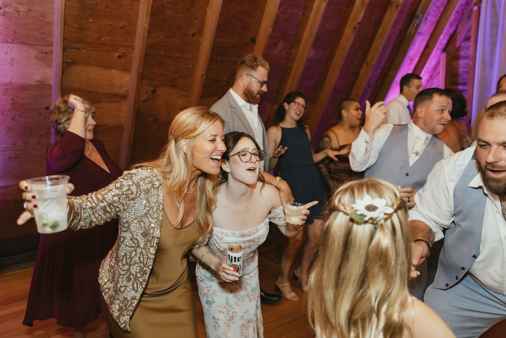 Wedding party dancing and celebrating on a dance floor illuminated with purple lighting.