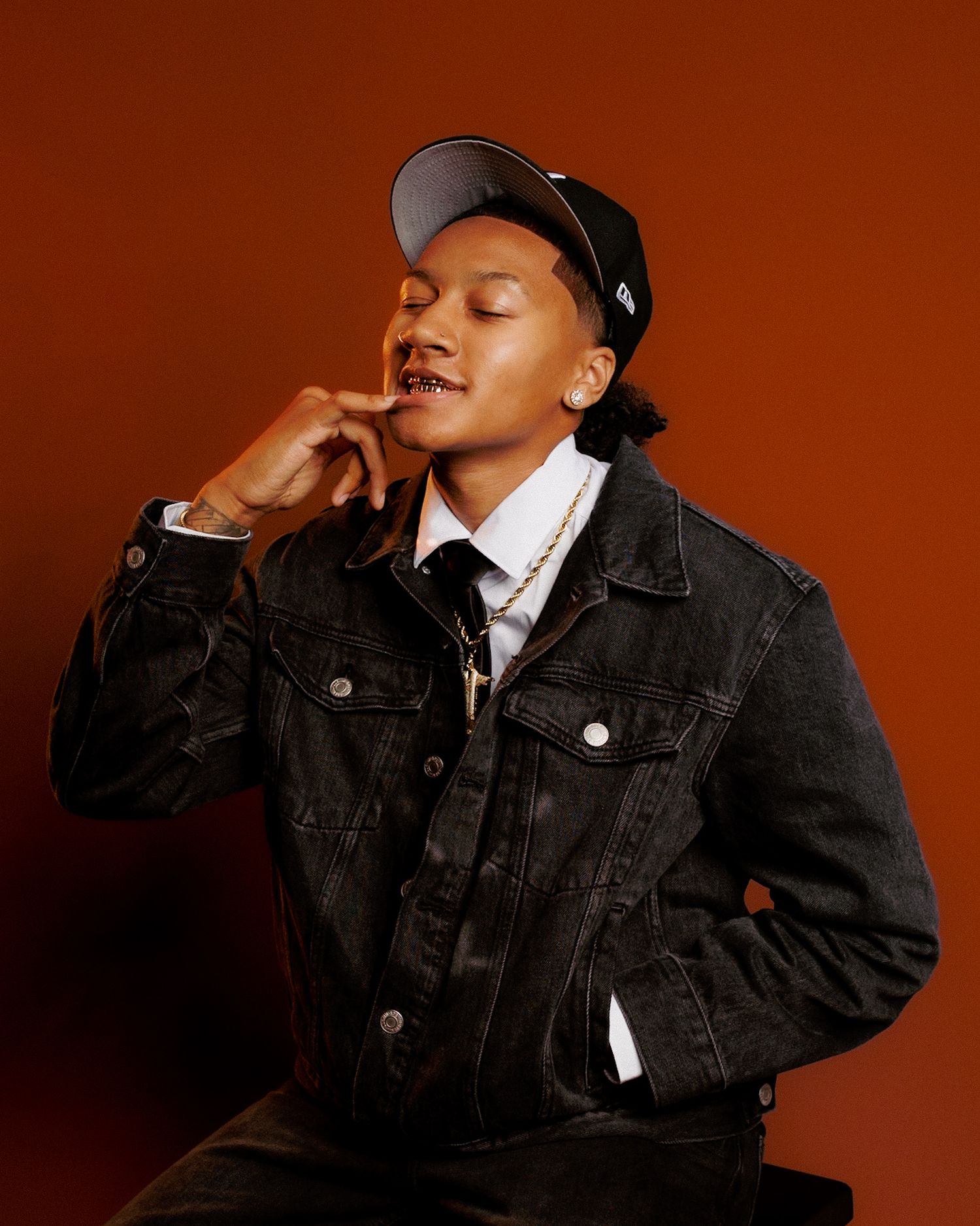 Person in black denim jacket and white shirt poses expressively against warm brown background in photo series.