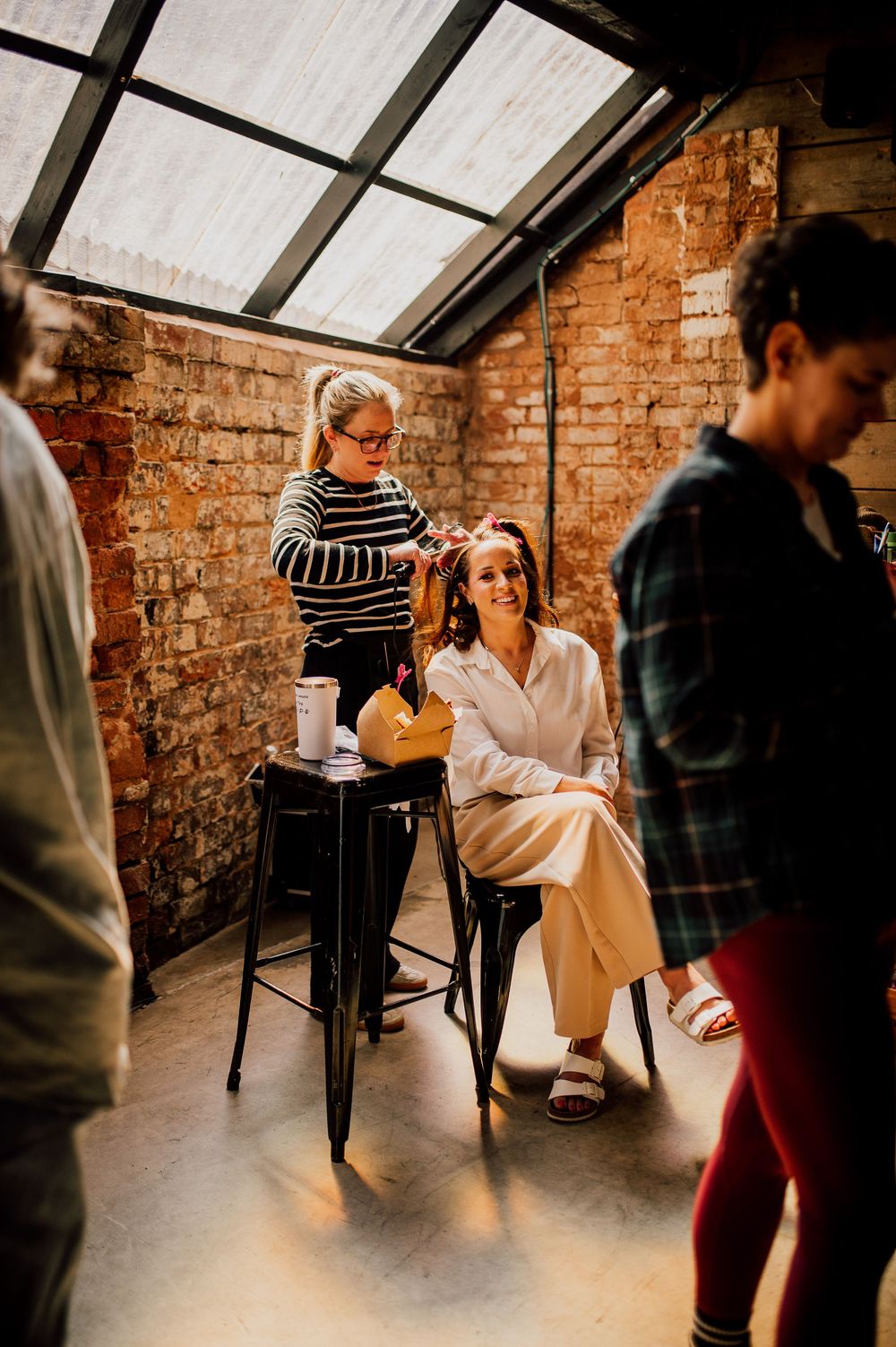People practicing dance moves in a rustic brick-walled studio space with natural light streaming through skylights.