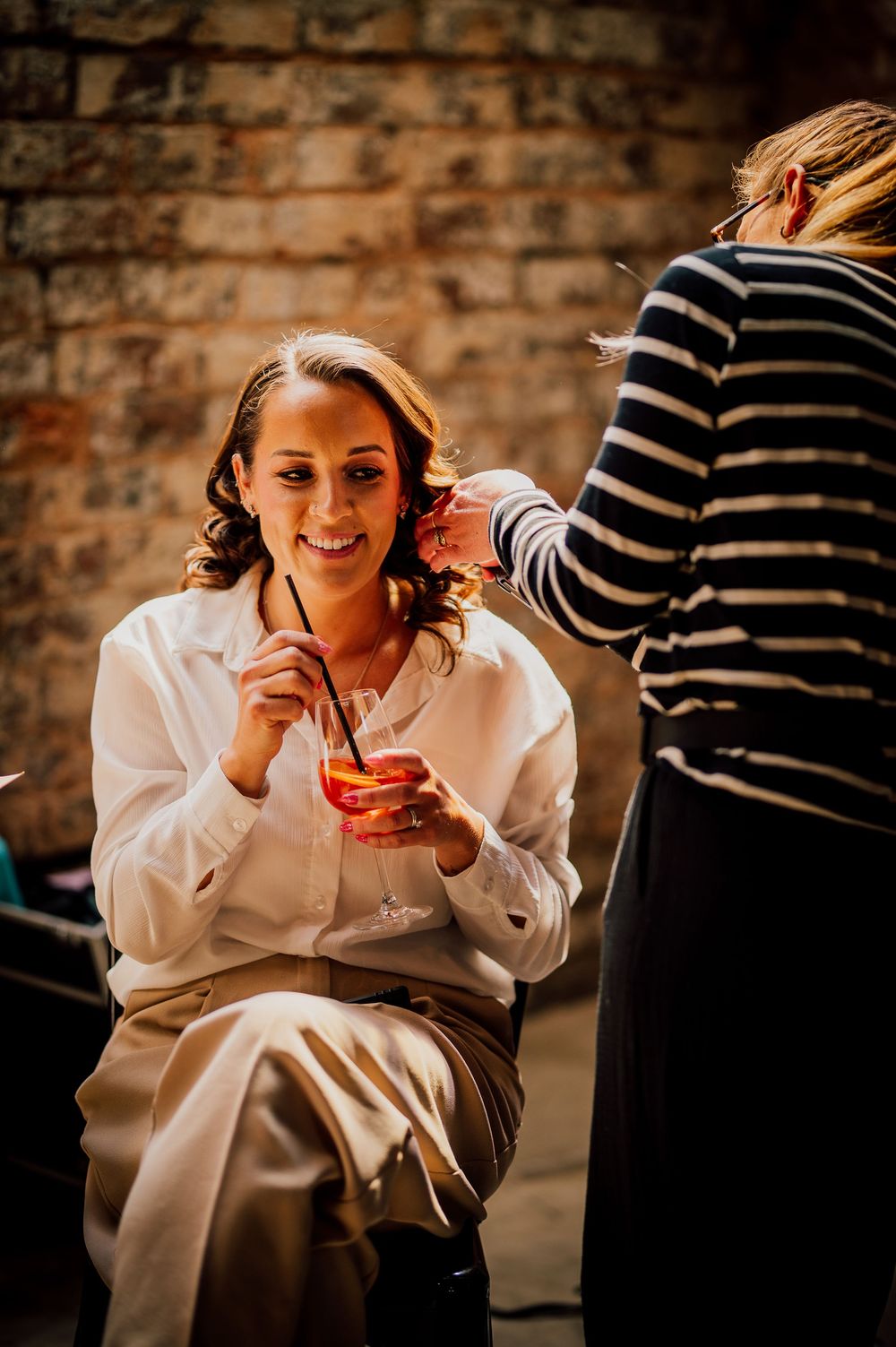Person in a white sweater enjoying a warm beverage in a cozy brick-walled setting.