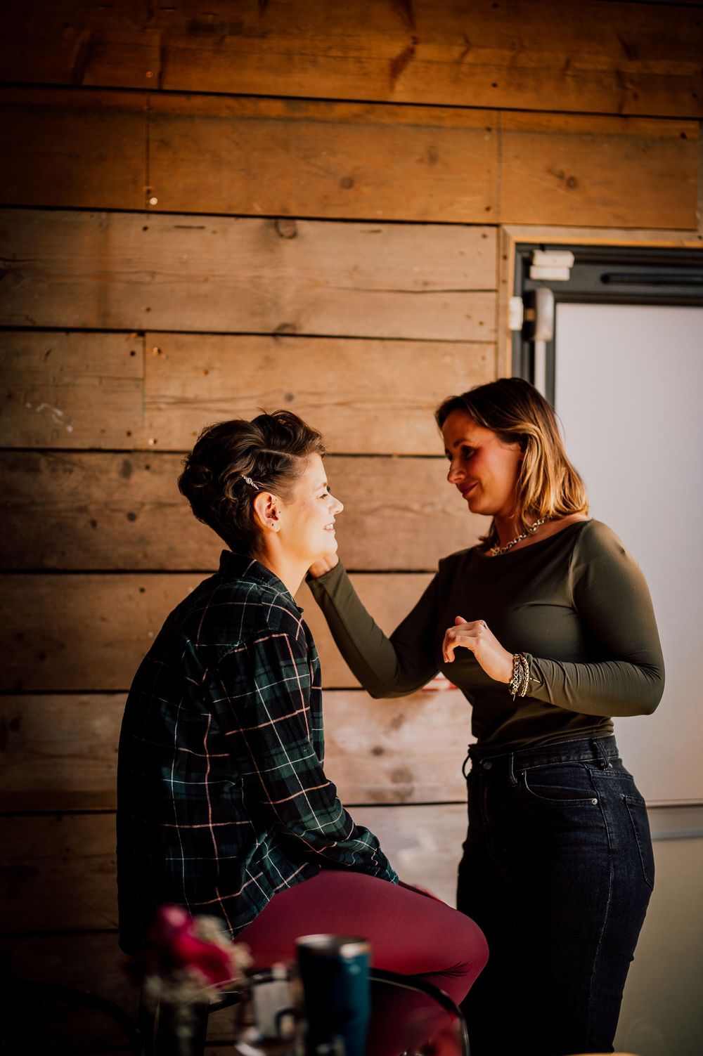 Two people share an intimate moment against a rustic wooden wall backdrop in warm lighting.