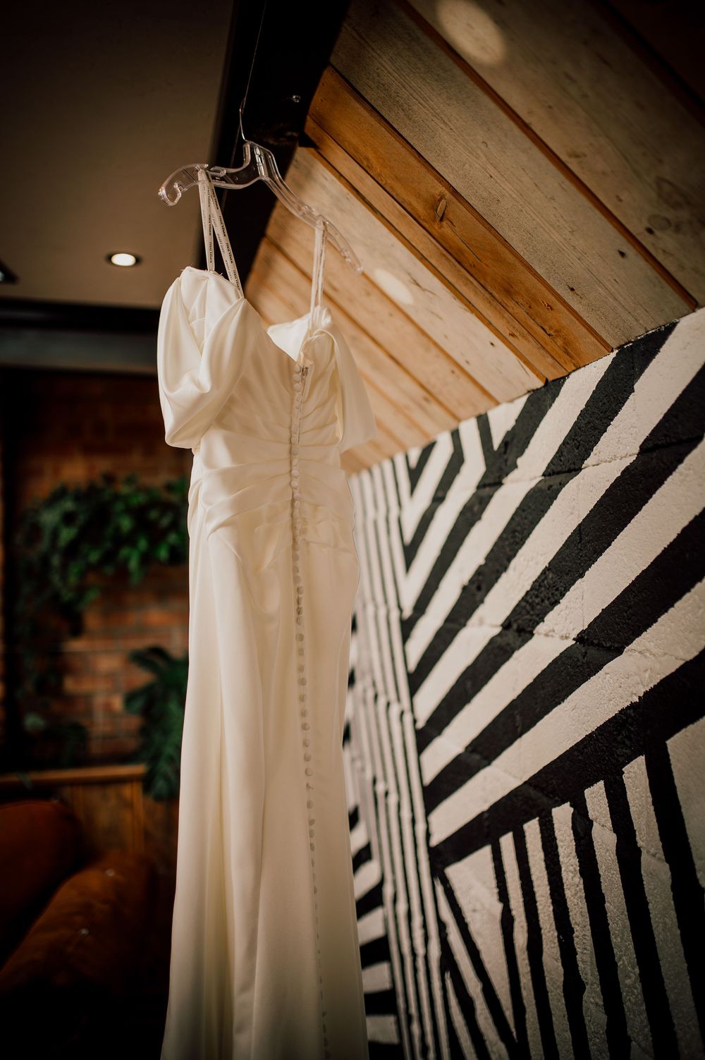 A white wedding dress hangs elegantly against a black and white striped backdrop in moody lighting.