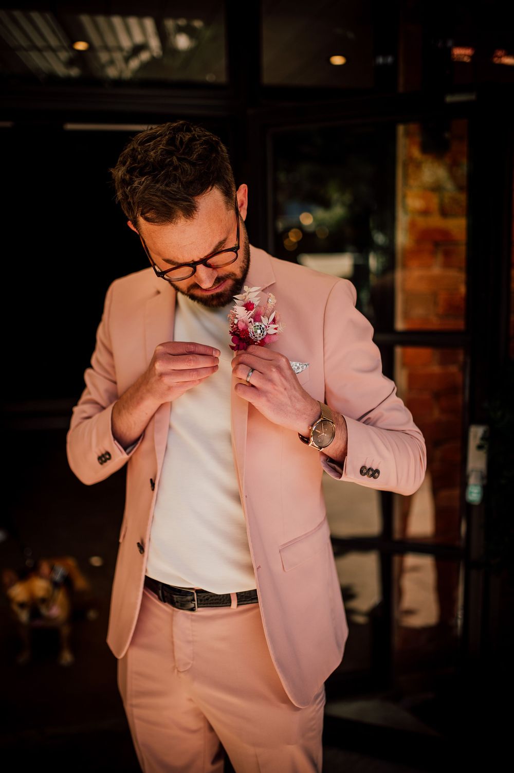 Person in pink suit jacket and white shirt laughing and wiping their face at what appears to be a restaurant or bar.
