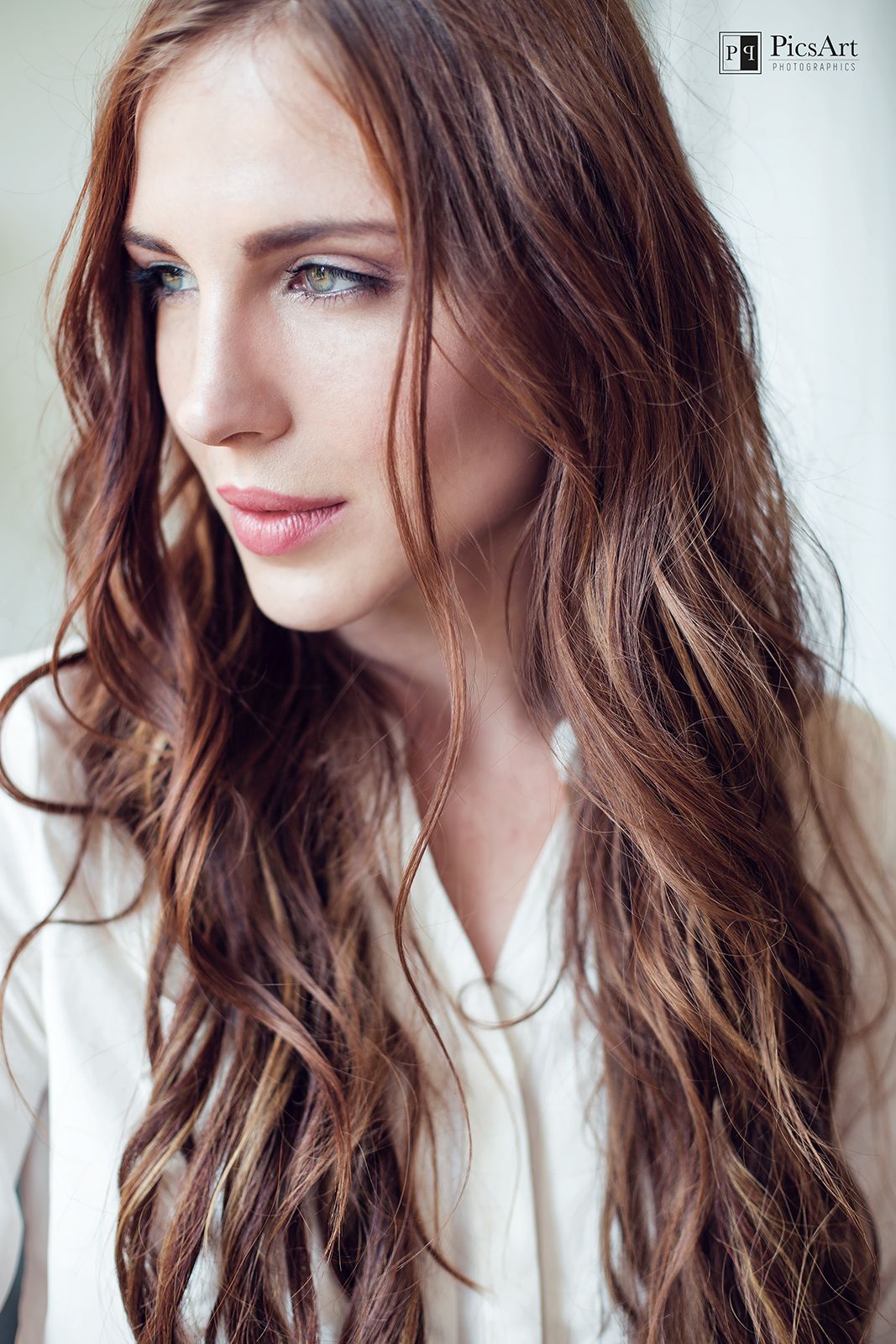Portrait of young woman with long wavy auburn hair and blue eyes in white blouse.