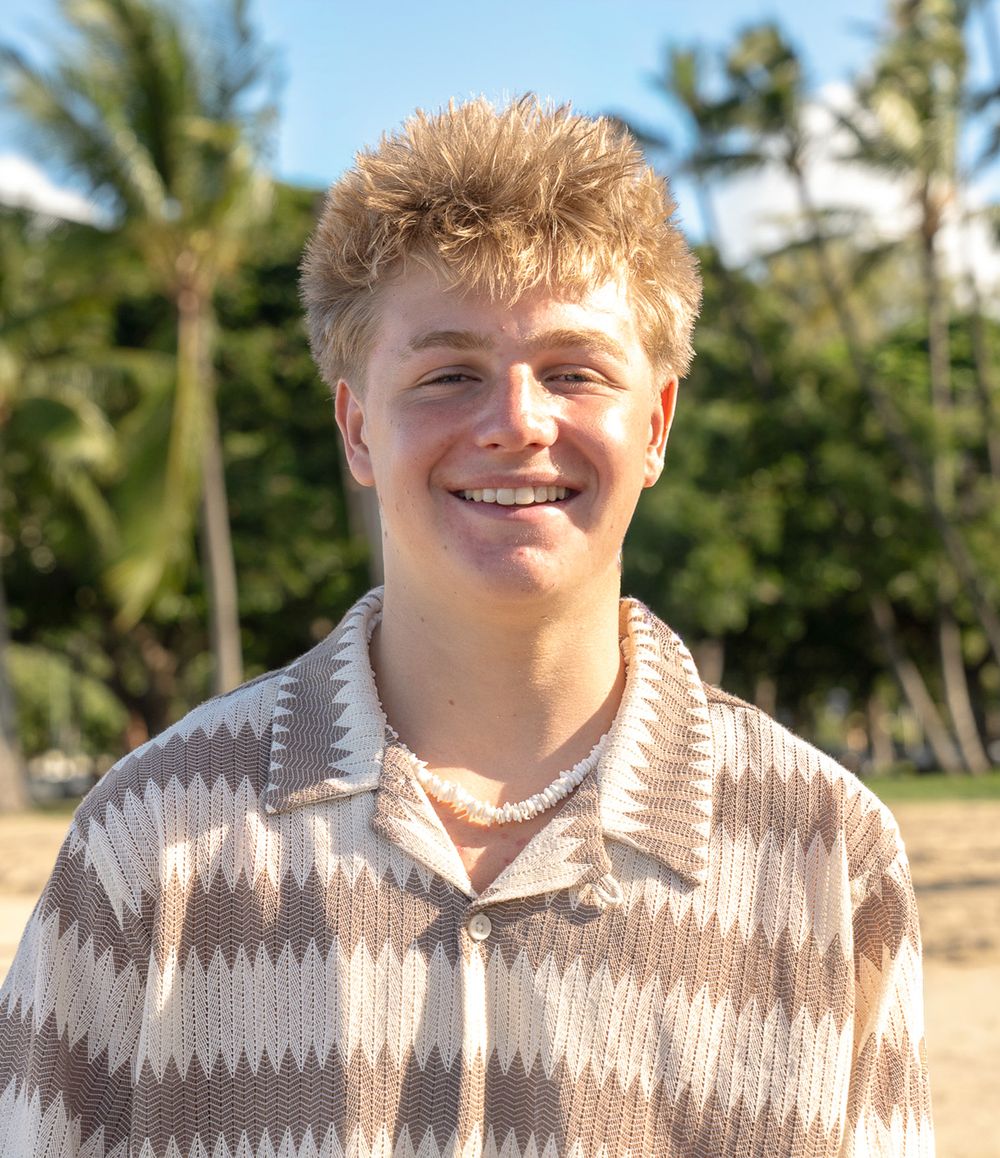 Person wearing a beige and white patterned sweater poses against a tropical outdoor background with palm trees.