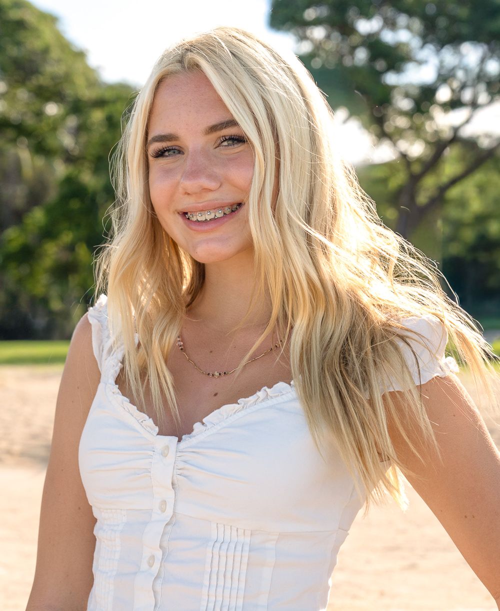 A person wearing a white summer dress smiles while standing outdoors in natural sunlight.