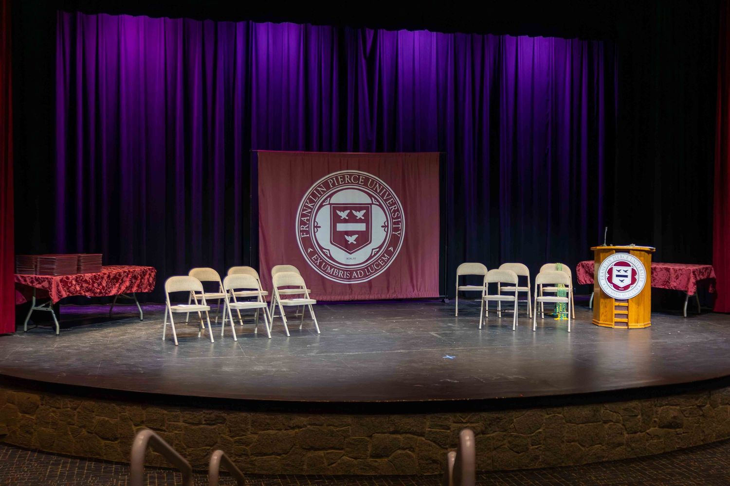 Empty stage setup with purple lighting and institutional banner displayed.