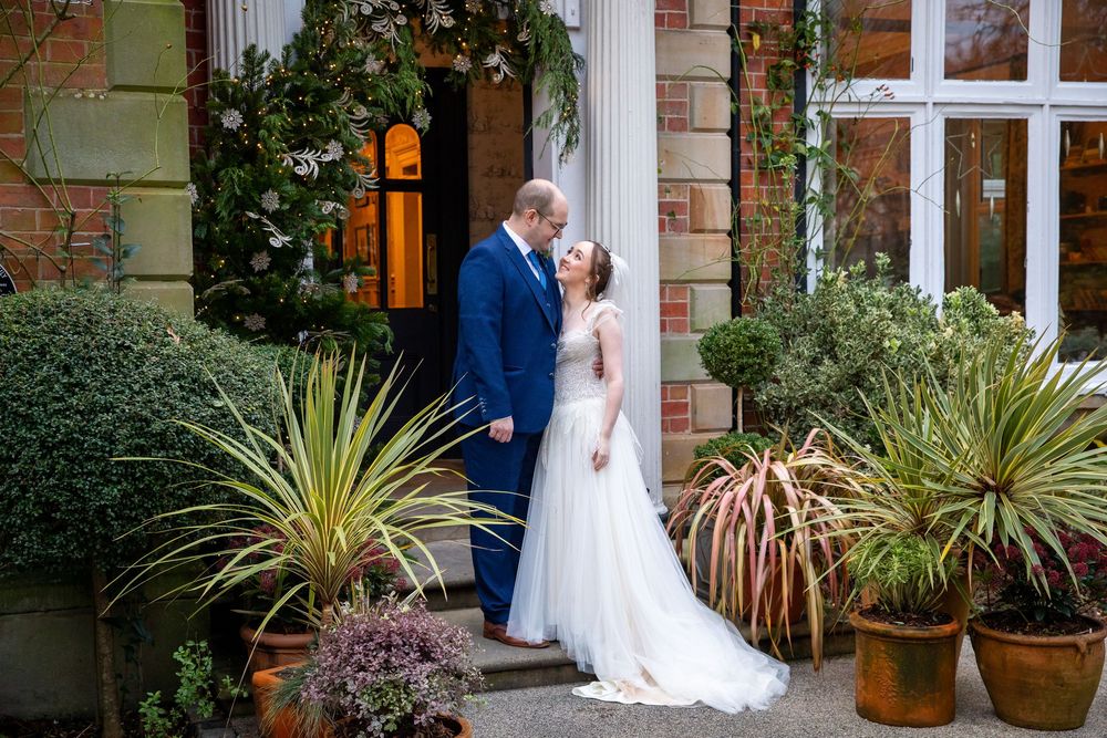 Bride and groom share a tender kiss surrounded by tropical plants at a brick manor.