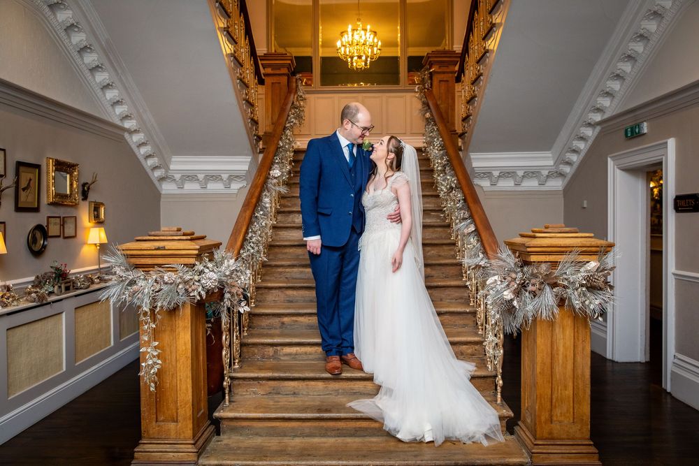 Bride and groom gaze at each other on a grand staircase adorned with festive garlands.