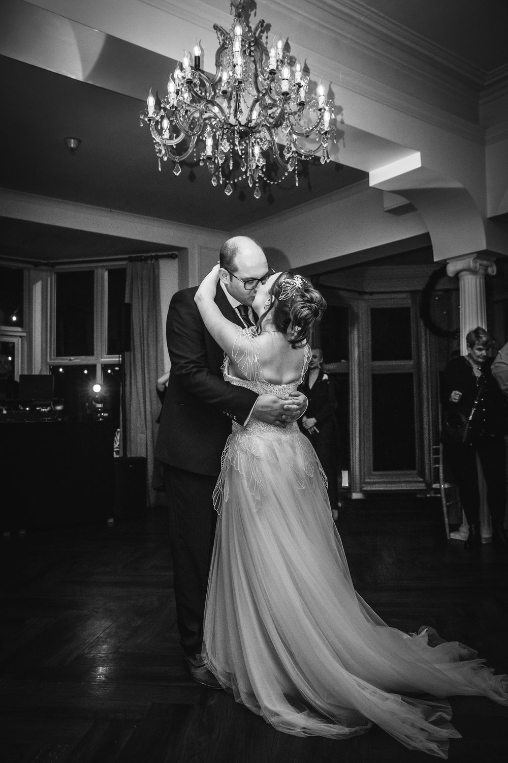 Black and white photo of bride and groom sharing first dance under chandelier.