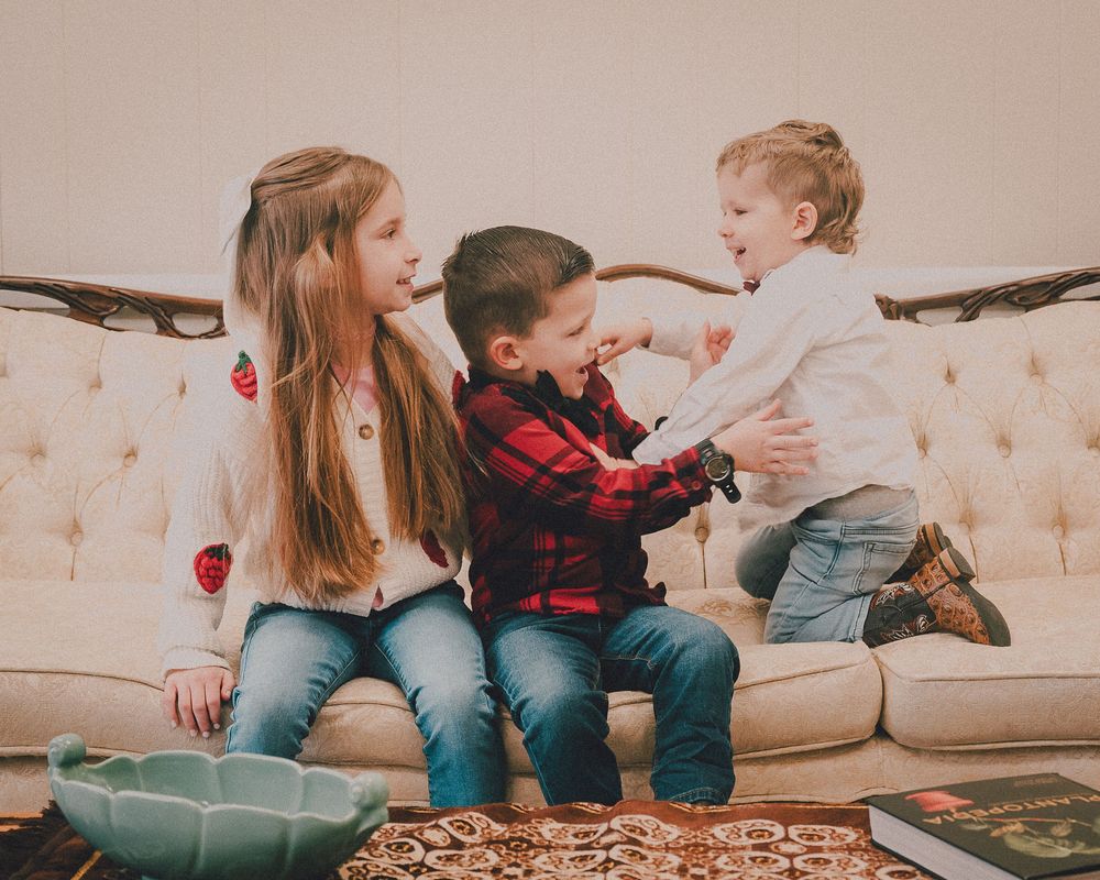 A family sits together on a cream colored couch playing and bonding in a warm living room setting.