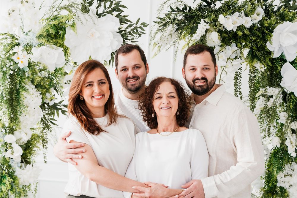 Family members wearing white outfits pose together against a floral backdrop with white flowers and greenery.