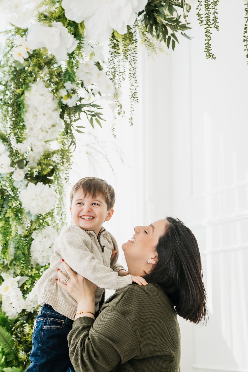 A joyful moment captured against a white floral backdrop with hanging greenery and delicate white flowers.