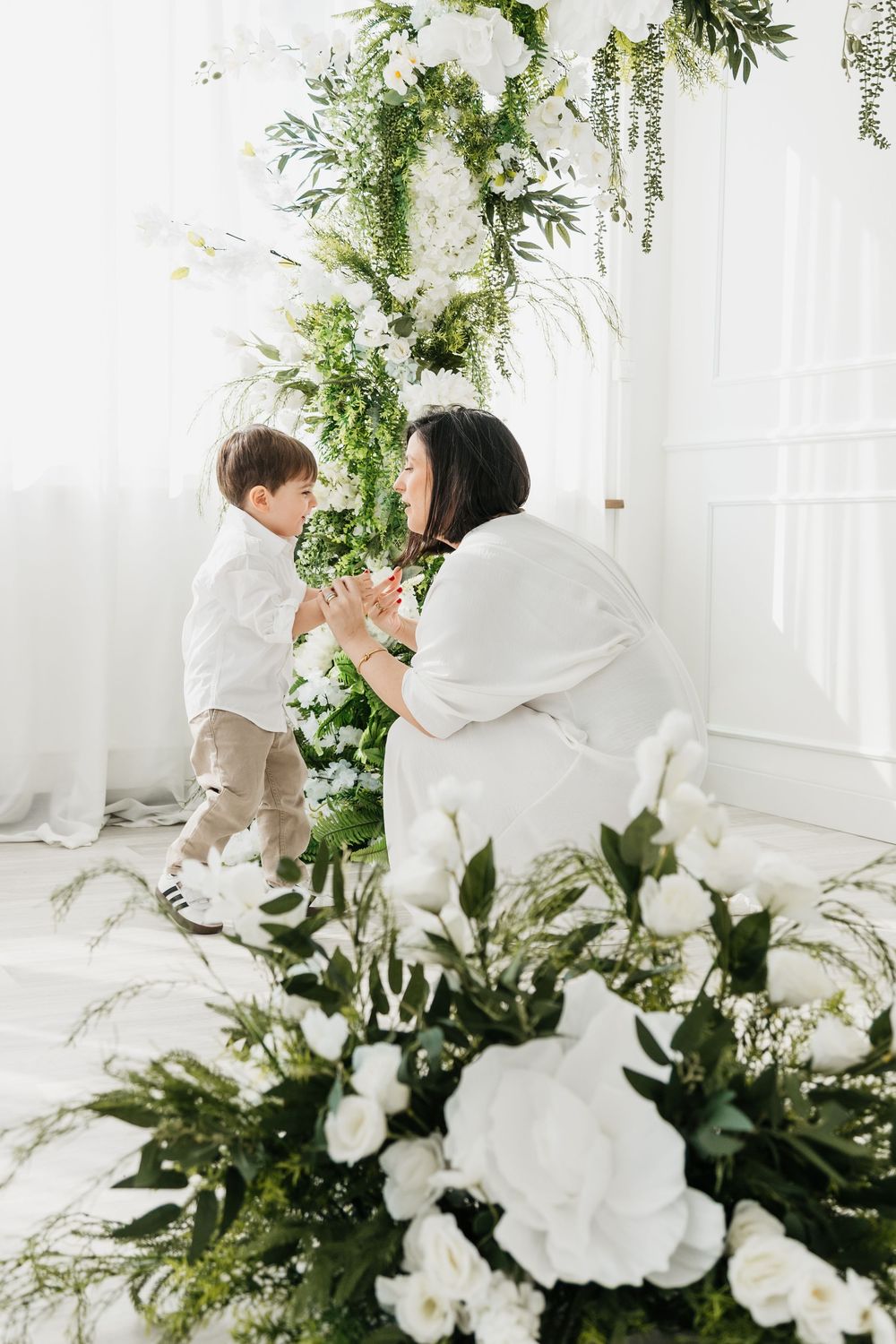Romantic wedding scene with white floral arrangements and greenery decorations in an elegant bright indoor setting.