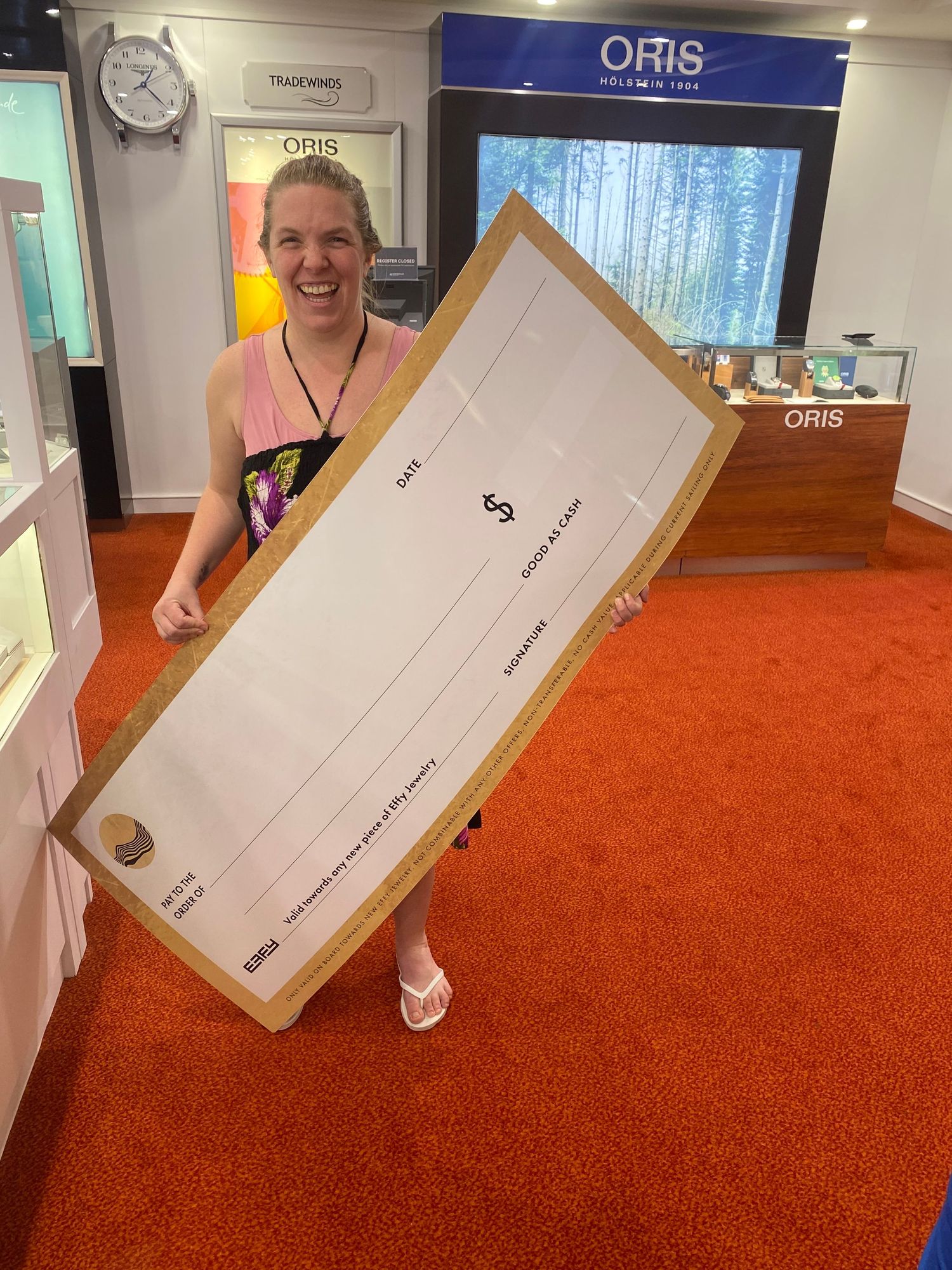 Excited woman holding oversized $1,000 prize check from ESFY dated 1/19/2026 in a cruise ship theater.
