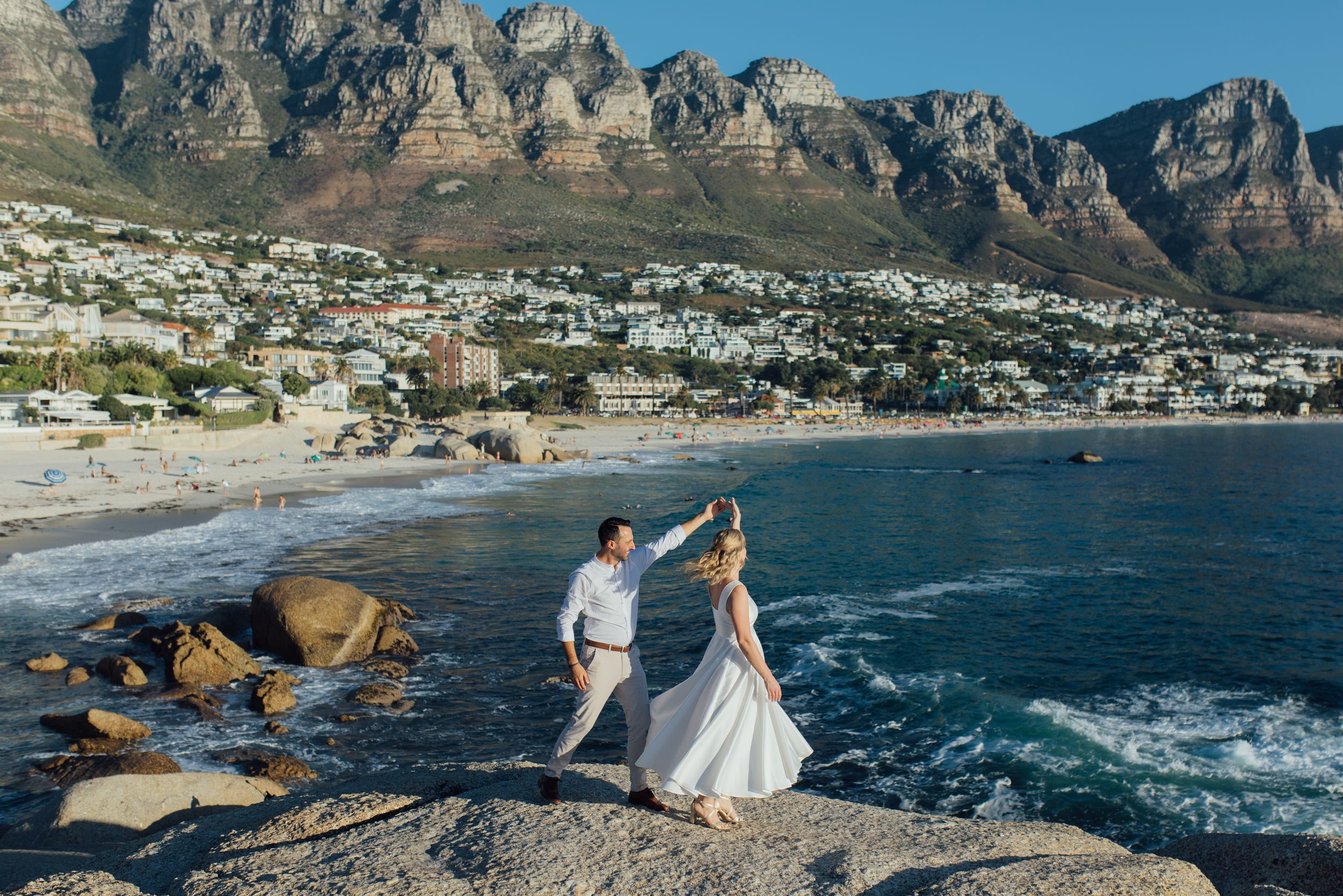 Couple dancing on rocky shore at Camps Bay beach with Twelve Apostles mountain backdrop in Cape Town.