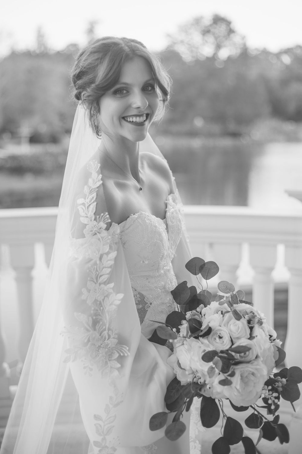A bride in a white lace wedding dress holds a romantic bouquet of white and burgundy flowers against a sunlit backdrop in Huntsville alabama
