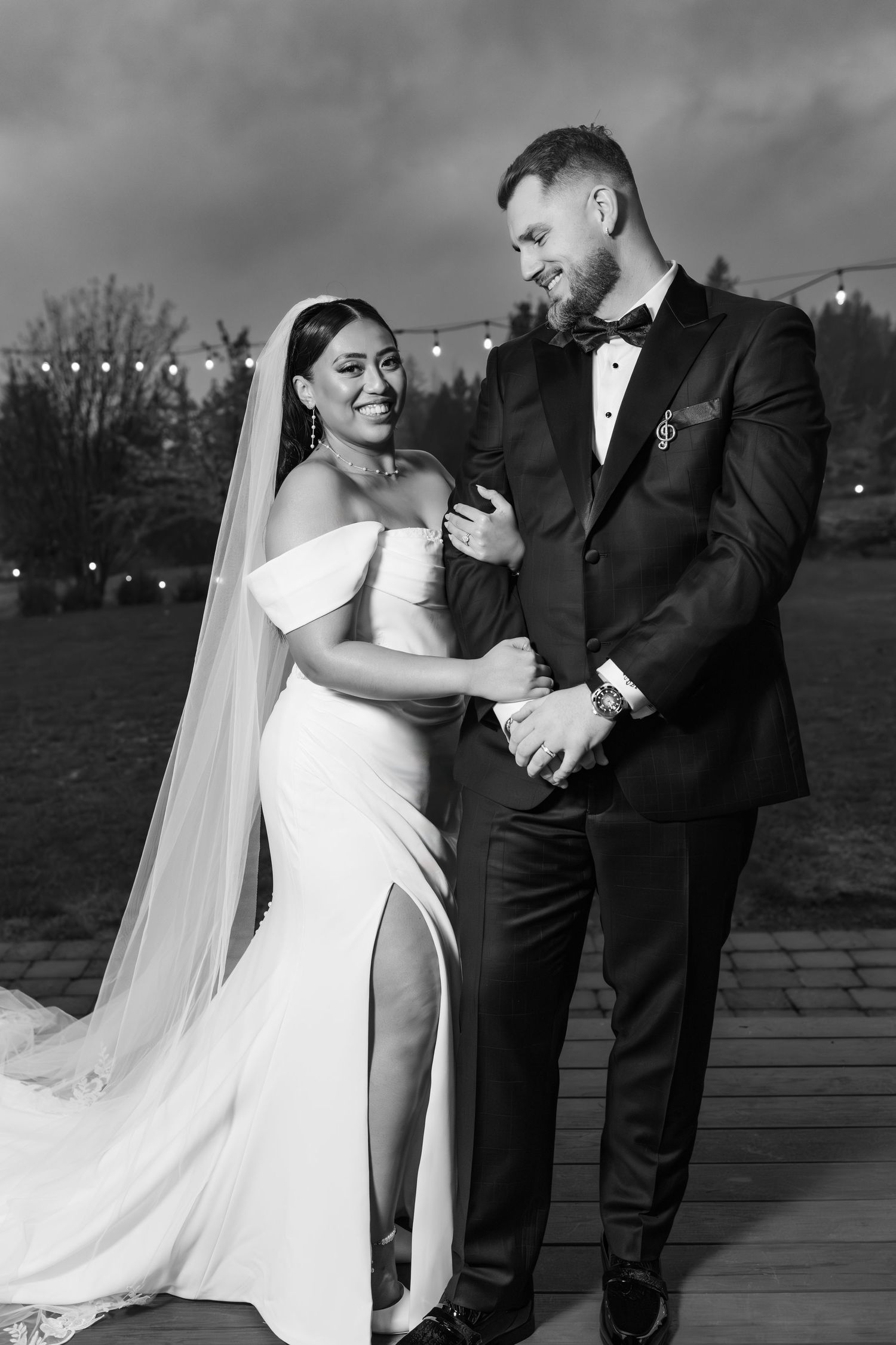 A bride and groom share a romantic moment during their wedding photo session on a deck with dramatic cloudy skies.