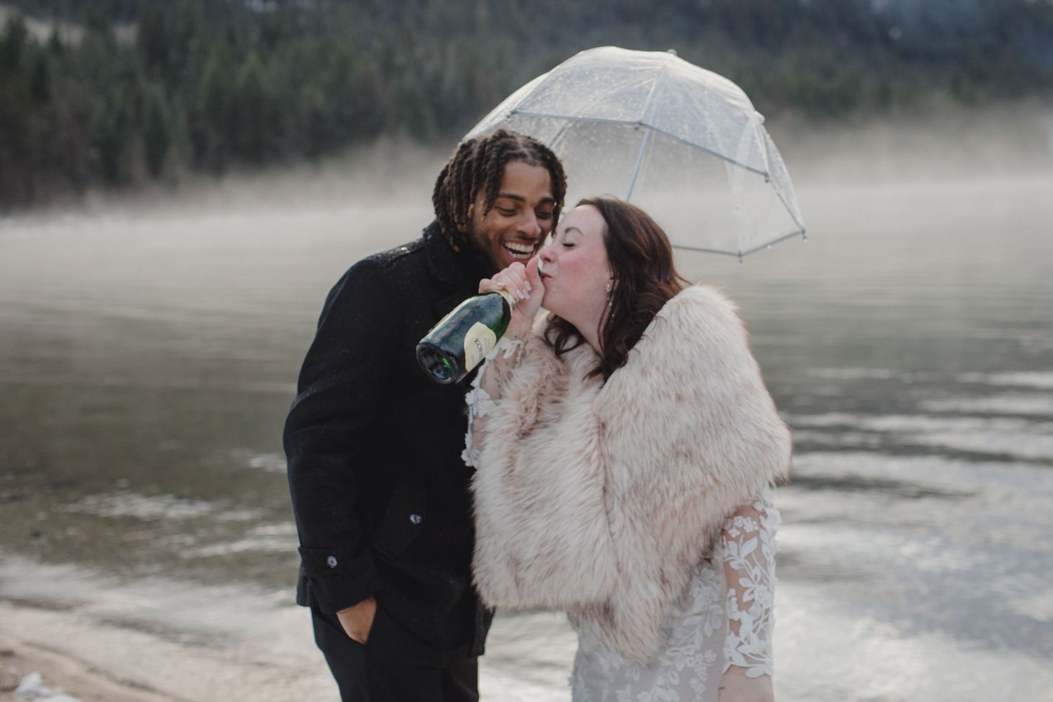 A couple shares a romantic kiss under a white umbrella in a misty outdoor setting.
