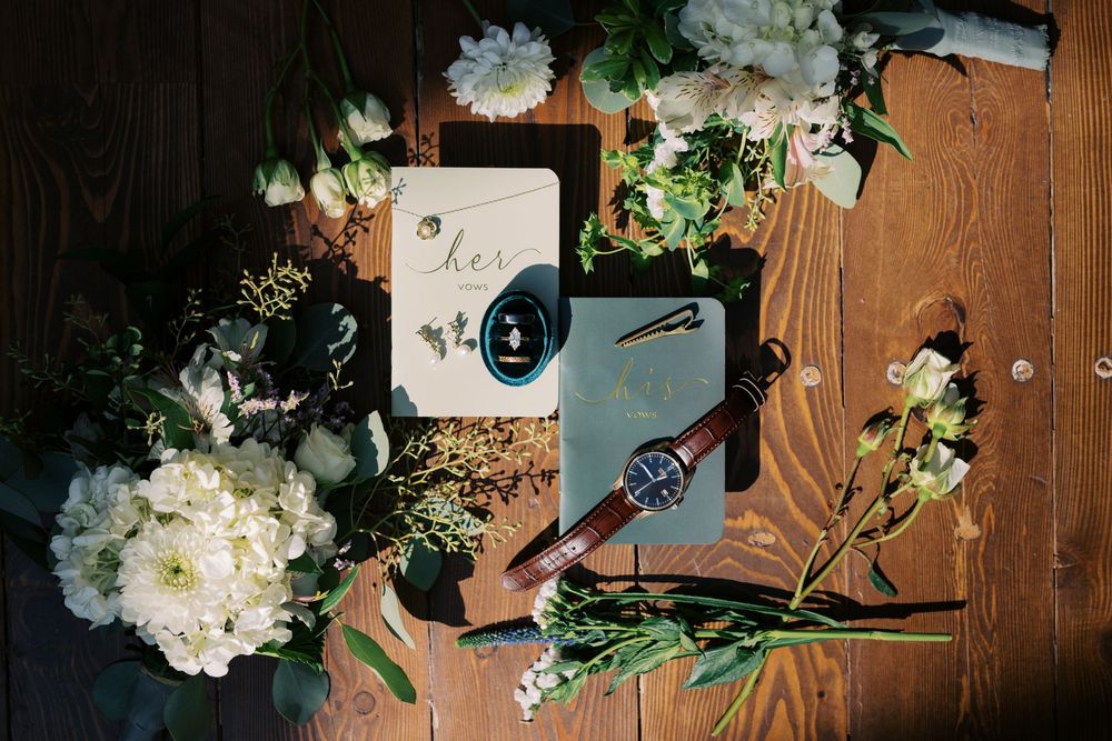 White floral arrangements with greenery decorate a rustic wooden wall with string lights creating a romantic ambiance.