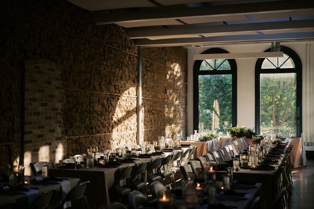 Elegant wedding reception setup in rustic stone room with arched windows and long tables decorated with candles.