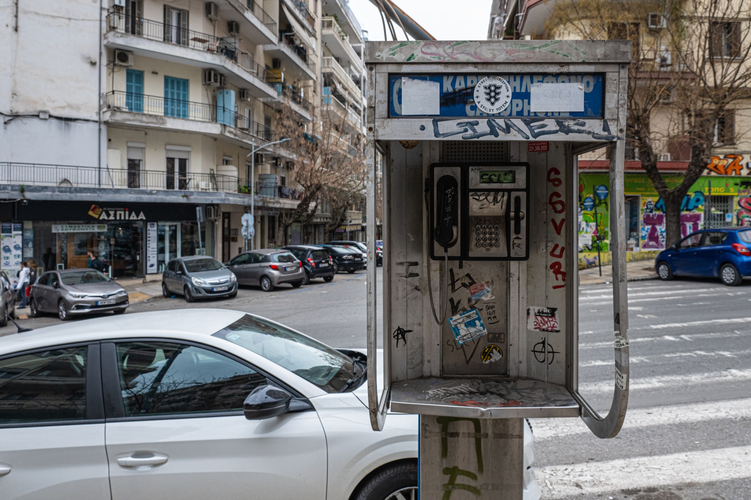 A street scene with parked cars, shops, and a public phone booth.