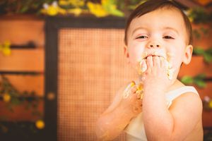 Adorable baby with food on face smiling and eating with hands outdoors in warm natural setting.