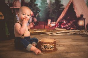 Baby boy named Carson sitting on floor with rustic log cake smash, camping themed birthday photo.