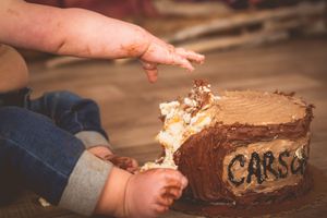 Baby smashing a chocolate cake labeled Carson during a first birthday cake smash photo session.