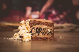 Close-up of a sliced chocolate layer cake with Carson written in frosting on a wooden surface.