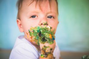 Cute toddler boy with colorful paint covering his hands and face during a fun messy art activity.