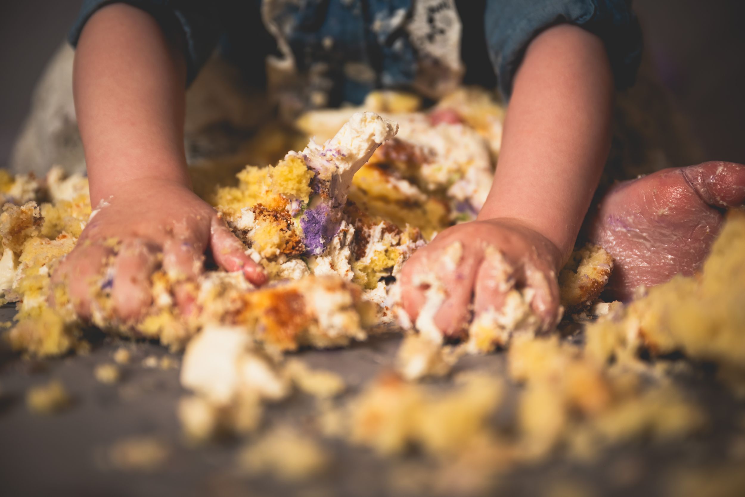 Close-up of baby hands smashing colorful first birthday cake during smash cake photo session.