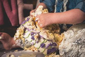Child smashing a decorated white and purple wedding cake with their hands at a celebration.