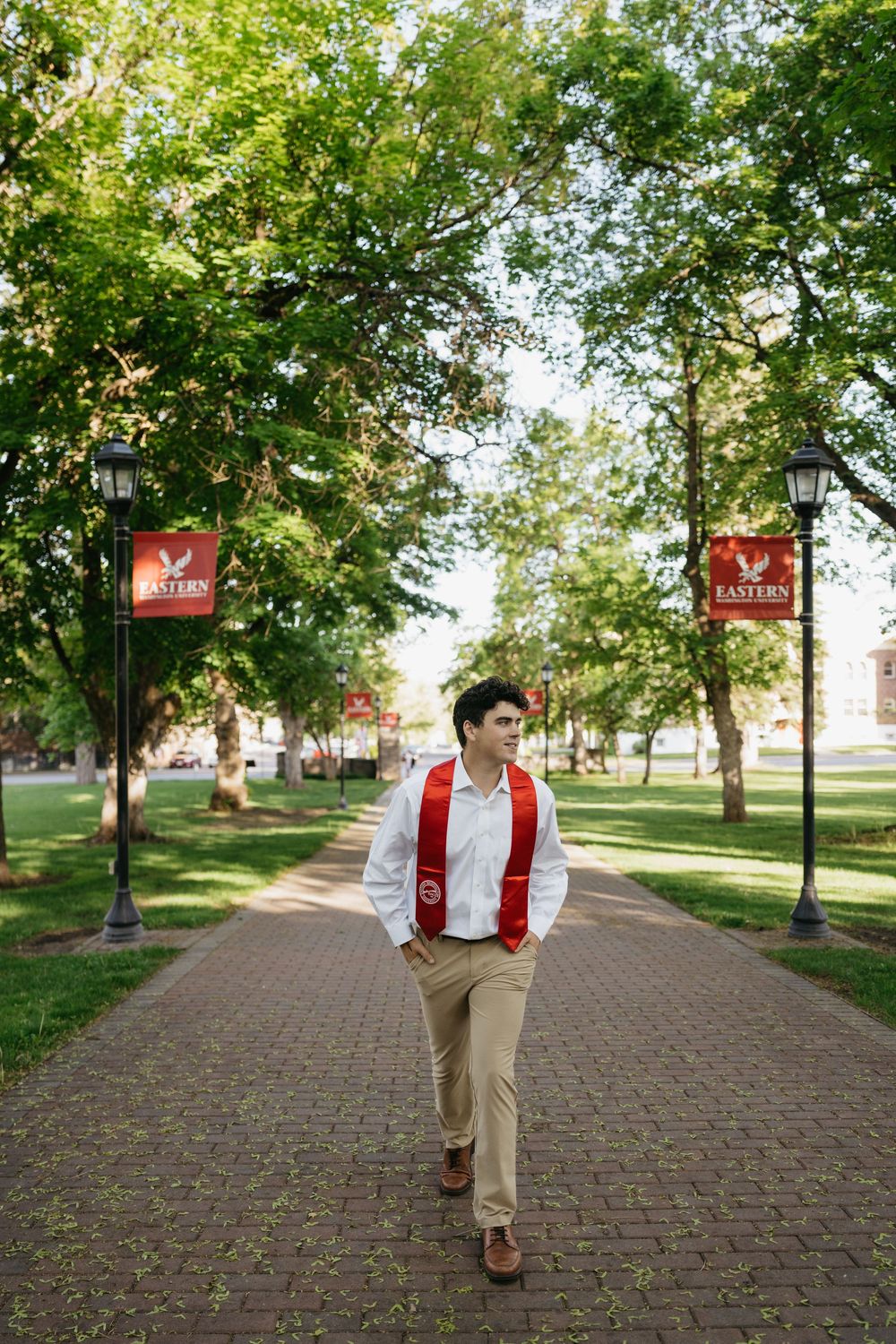 A graduate walks confidently on a brick path at Eastern University, wearing a red stole over a white shirt.