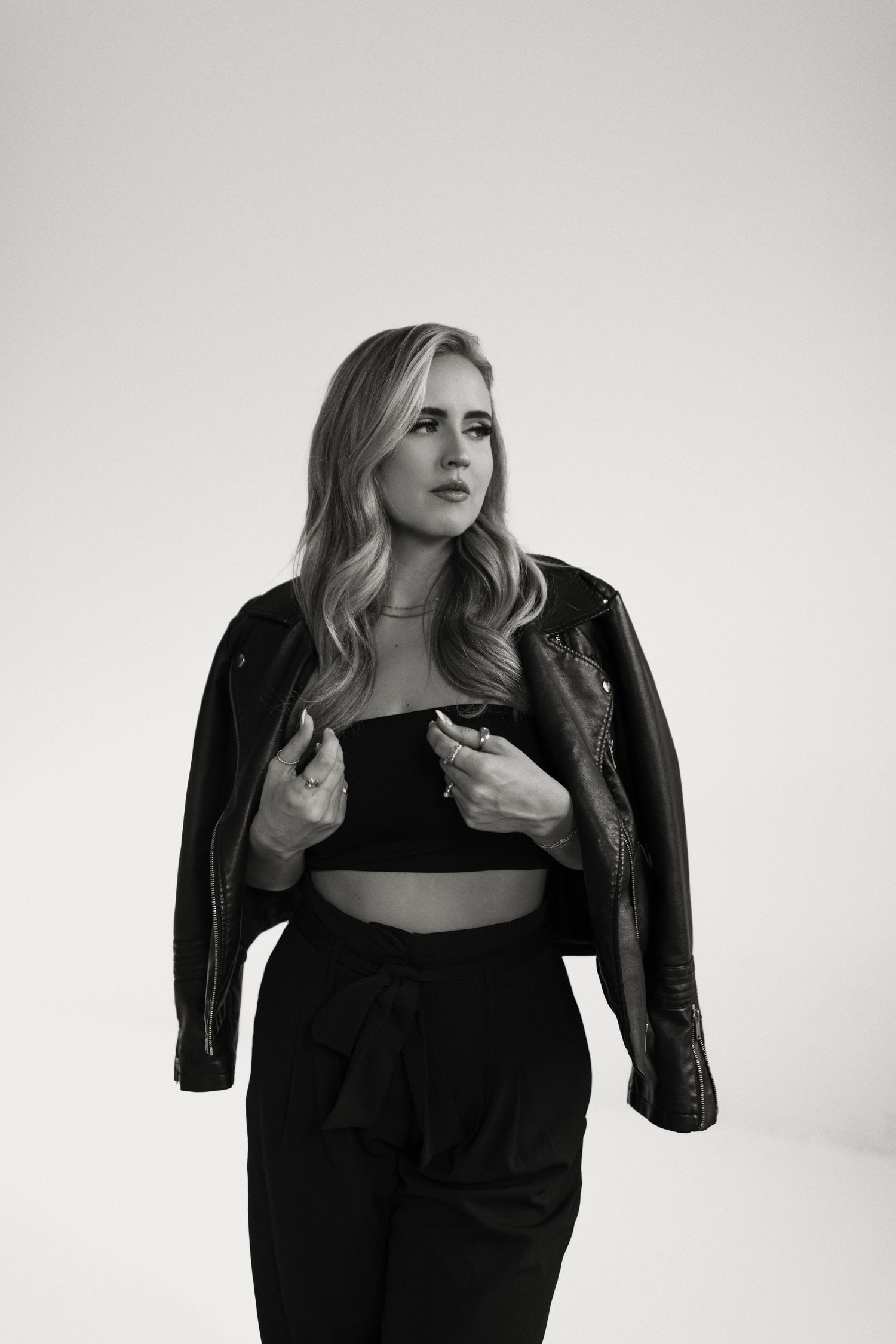Fashion model wearing black leather jacket and top poses against white background in three artistic shots.