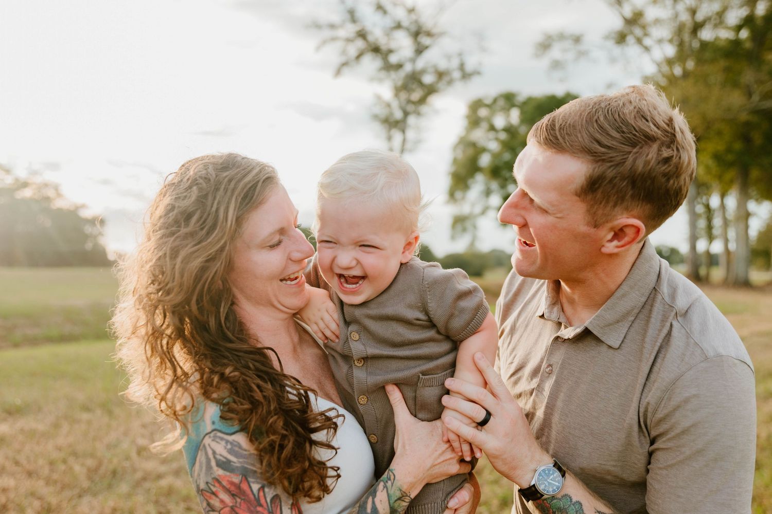Family laughing together during sunset photo session in open field.